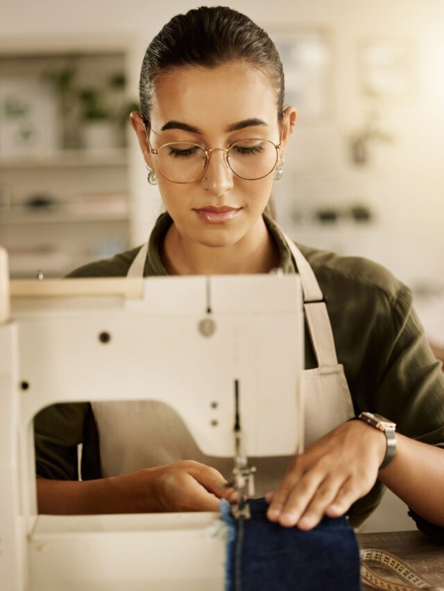 Mixed race designer sewing a piece of denim. Young tailor using a sewing machine. Creative businesswoman stitching a piece of fabric. Fashion designer sewing a piece of material